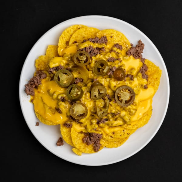Burger Bite nachos with melted cheese, ground beef, and sliced jalapeños on a white plate.