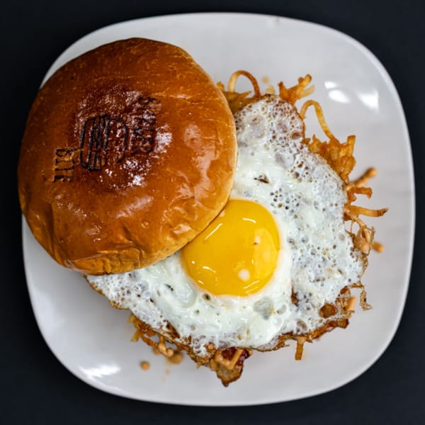 Burger Bite burger with a fried egg and crispy hash browns on a white plate.
