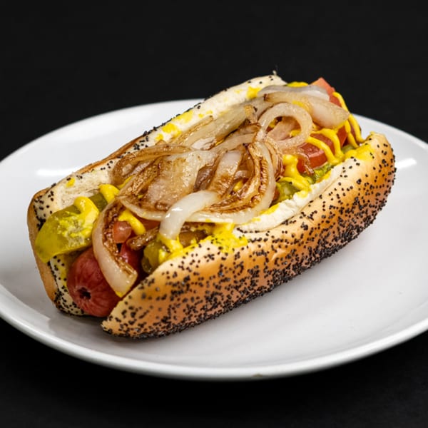 A hot dog in a poppy seed bun, topped with grilled onions, mustard, relish, and tomatoes.