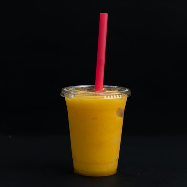 A vibrant yellow mango smoothie in a clear plastic cup with a red straw against a dark background.